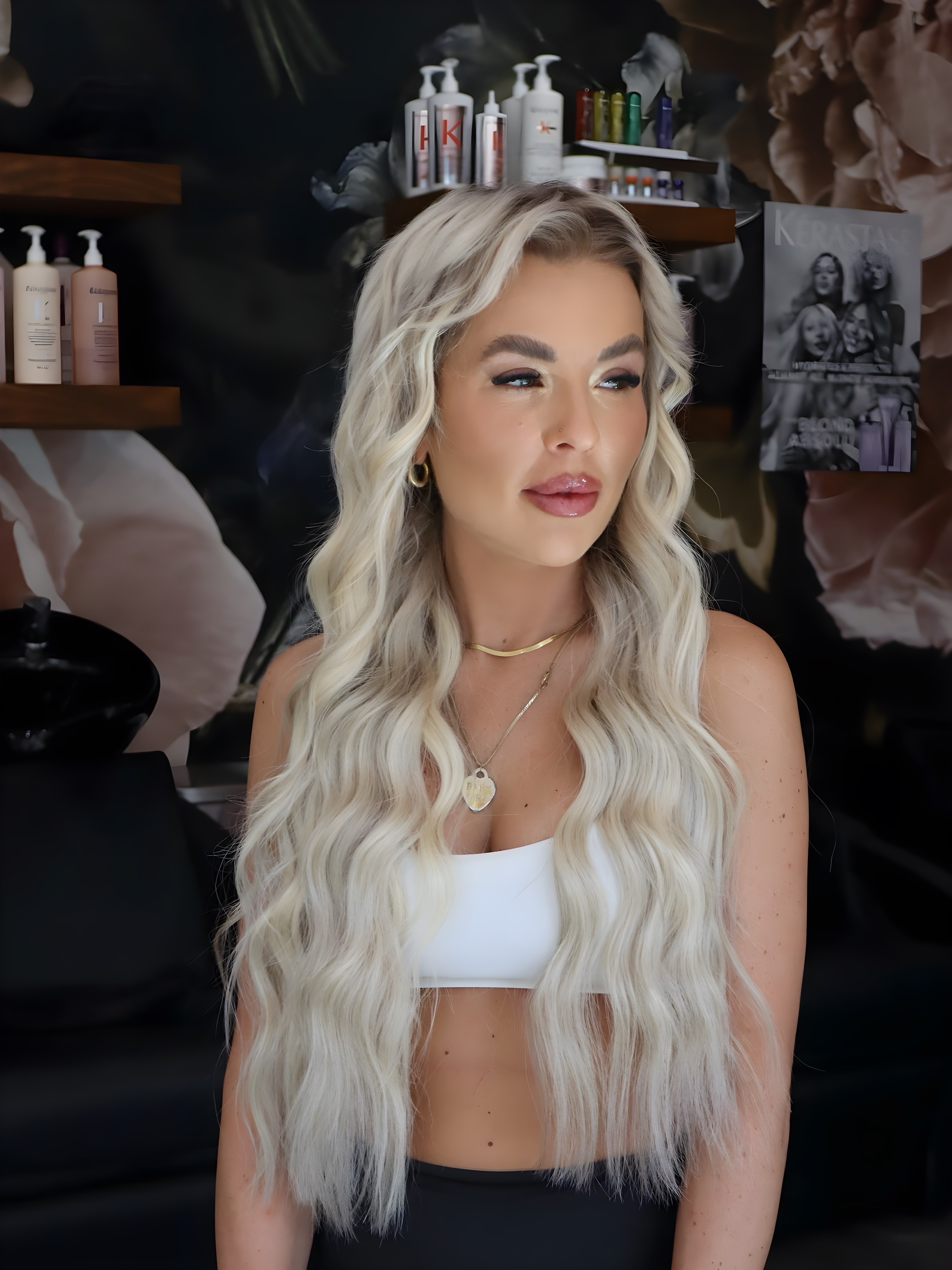 Client with icy blonde hand tied extensions in front of the floral wall at Bloom Salon ATX